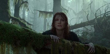 Movie still from “Jurassic World Dominion” (2022), directed by Colin Trevorrow – A woman standing next to a tree in the woods; Medium shot, Low angle