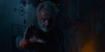 Movie still from “Jurassic World Dominion” (2022), directed by Colin Trevorrow – An older man with grey hair is holding his hand out; Close Up shot, Over the shoulder angle