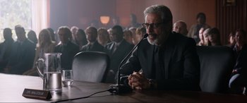 Movie still from “Jurassic World: Fallen Kingdom” (2018), directed by J.A. Bayona – A man sitting in front of microphones in a courtroom; Medium shot, Low angle