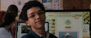 Movie still from “Jurassic World: Fallen Kingdom” (2018), directed by J.A. Bayona – A young man wearing glasses is smiling for the camera in front of a computer screen; Close Up shot, Over the shoulder angle