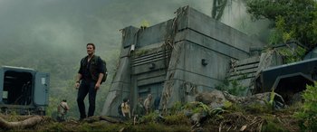 Movie still from “Jurassic World: Fallen Kingdom” (2018), directed by J.A. Bayona – A group of people standing next to a building on top of a hill; Wide shot, Low angle