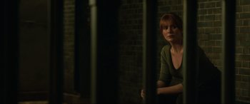 Movie still from “Jurassic World: Fallen Kingdom” (2018), directed by J.A. Bayona – A woman sitting in a dark room next to a brick wall; Medium shot, Over the shoulder angle