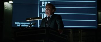 Movie still from “Jurassic World: Fallen Kingdom” (2018), directed by J.A. Bayona – A man in a suit is speaking at a podium; Medium shot, Low angle