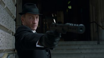 Movie still from “Justice League” (2017), directed by Zack Snyder – A man wearing a hat and holding a gun in his hand; Close Up shot, Low angle