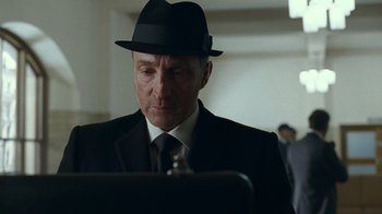 Movie still from “Justice League” (2017), directed by Zack Snyder – A man in a suit and a hat looking at a computer screen; Close Up shot, Low angle