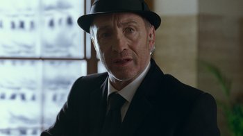 Movie still from “Justice League” (2017), directed by Zack Snyder – A person wearing a suit and a hat; Close Up shot, Low angle