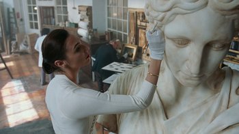 Movie still from “Justice League” (2017), directed by Zack Snyder – A woman in white shirt painting a statue of a woman; Close Up shot, Over the shoulder angle