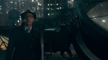 Movie still from “Justice League” (2017), directed by Zack Snyder – An older man in a suit and hat standing in front of an old movie camera; Medium shot, Low angle