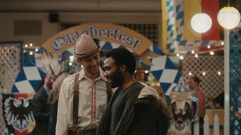 Movie still from “Atlanta” (2016), created by Donald Glover – Two men standing next to each other in front of an oktoberfest sign; Medium shot, Over the shoulder angle