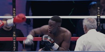 Movie still from “KSI: In Real Life” (2023), directed by Wes Pollitt – A man sitting in the corner of a boxing ring; Medium shot, High angle