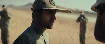 Movie still from “Kandahar” (2023), directed by Ric Roman Waugh – A man wearing a hat in the middle of a field; Close Up shot, Over the shoulder angle