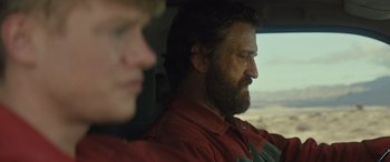 Movie still from “Kandahar” (2023), directed by Ric Roman Waugh – A man sitting in a car with another man behind him; Close Up shot, Over the shoulder angle