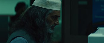 Movie still from “Kandahar” (2023), directed by Ric Roman Waugh – A person with long hair wearing a hat; Close Up shot, Over the shoulder angle
