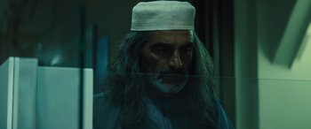 Movie still from “Kandahar” (2023), directed by Ric Roman Waugh – A man with long grey hair and a white hat; Close Up shot, Low angle