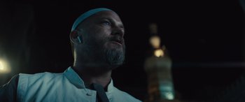 Movie still from “Kandahar” (2023), directed by Ric Roman Waugh – A man with a beard wearing a white shirt; Close Up shot, Low angle