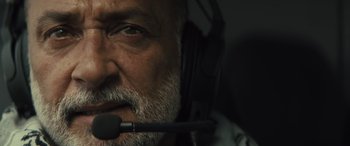 Movie still from “Kandahar” (2023), directed by Ric Roman Waugh – An older man with a beard wearing a headset; Close Up shot, Low angle