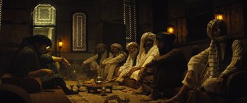 Movie still from “Kandahar” (2023), directed by Ric Roman Waugh – A group of men sitting around a fire pit; Wide shot, Low angle