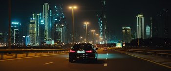 Movie still from “Kandahar” (2023), directed by Ric Roman Waugh – A car driving down a street at night with lights on; Extreme Wide shot, High angle