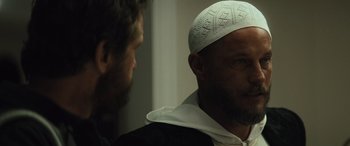 Movie still from “Kandahar” (2023), directed by Ric Roman Waugh – A man wearing a white hat with a beard; Close Up shot, Over the shoulder angle