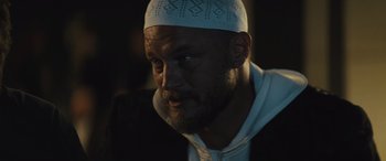 Movie still from “Kandahar” (2023), directed by Ric Roman Waugh – A person with a beard wearing a hat; Close Up shot, Low angle