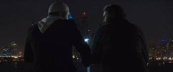 Movie still from “Kandahar” (2023), directed by Ric Roman Waugh – Two people holding hands in front of a city skyline at night; Medium shot, Over the shoulder angle