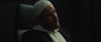 Movie still from “Kandahar” (2023), directed by Ric Roman Waugh – A man with a beard wearing a white hat; Close Up shot, Low angle