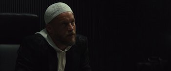 Movie still from “Kandahar” (2023), directed by Ric Roman Waugh – A man with a beard wearing a white hat; Close Up shot, Low angle