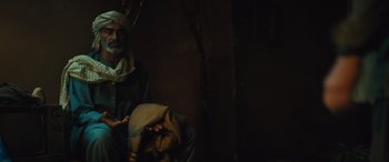 Movie still from “Kandahar” (2023), directed by Ric Roman Waugh – A man sitting in a dark room holding a bag; Medium shot, Over the shoulder angle