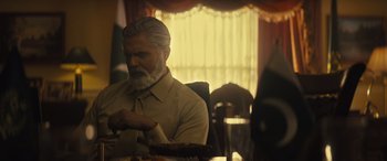 Movie still from “Kandahar” (2023), directed by Ric Roman Waugh – An older man sitting at a dinner table; Medium shot, Low angle