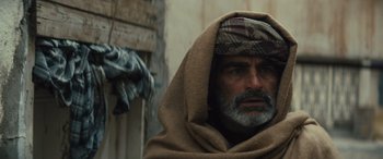 Movie still from “Kandahar” (2023), directed by Ric Roman Waugh – A man with a beard and a head covering; Close Up shot, Over the shoulder angle