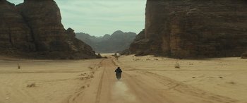 Movie still from “Kandahar” (2023), directed by Ric Roman Waugh – A person riding a motorcycle down a dirt road; Extreme Wide shot, High angle