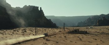 Movie still from “Kandahar” (2023), directed by Ric Roman Waugh – A truck driving down a dirt road in the middle of the desert; Extreme Wide shot, High angle
