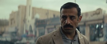 Movie still from “Kandahar” (2023), directed by Ric Roman Waugh – A person wearing a suit and tie; Close Up shot, Over the shoulder angle