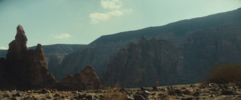Movie still from “Kandahar” (2023), directed by Ric Roman Waugh – A person standing on top of a hill near some rocks; Extreme Wide shot, Low angle