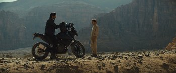 Movie still from “Kandahar” (2023), directed by Ric Roman Waugh – Two men standing next to a motorcycle in the desert; Wide shot, Over the shoulder angle