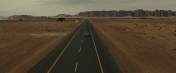 Movie still from “Kandahar” (2023), directed by Ric Roman Waugh – A car driving down the middle of an empty road; Extreme Wide shot, High angle