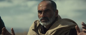 Movie still from “Kandahar” (2023), directed by Ric Roman Waugh – An older man with a beard and a tie; Close Up shot, Over the shoulder angle