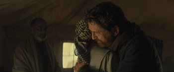 Movie still from “Kandahar” (2023), directed by Ric Roman Waugh – A man holding a stuffed animal in his arms; Medium shot, Over the shoulder angle