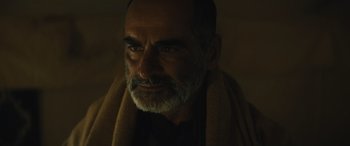 Movie still from “Kandahar” (2023), directed by Ric Roman Waugh – A man with a gray beard and a towel around his neck; Close Up shot, Over the shoulder angle