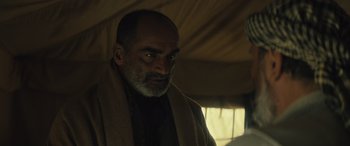 Movie still from “Kandahar” (2023), directed by Ric Roman Waugh – A man with a beard and a towel around his neck; Close Up shot, Over the shoulder angle