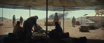 Movie still from “Kandahar” (2023), directed by Ric Roman Waugh – A group of people sitting under a tent in the desert; Wide shot, Over the shoulder angle