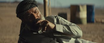 Movie still from “Kandahar” (2023), directed by Ric Roman Waugh – An older man smoking a cigarette while wearing a hat; Close Up shot, Low angle