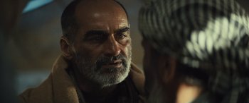 Movie still from “Kandahar” (2023), directed by Ric Roman Waugh – An old man with a beard and a mustache is talking to another man; Close Up shot, Over the shoulder angle