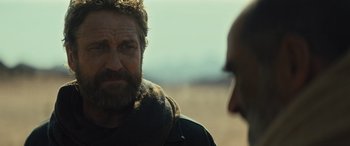 Movie still from “Kandahar” (2023), directed by Ric Roman Waugh – A man with a beard is looking at another man in a field; Close Up shot, Over the shoulder angle