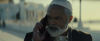 Movie still from “Kandahar” (2023), directed by Ric Roman Waugh – An older man with a white beard talking on a cell phone; Close Up shot, Low angle
