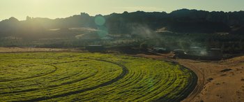 Movie still from “Kandahar” (2023), directed by Ric Roman Waugh – A field of green grass near a mountain range; Extreme Wide shot, High angle