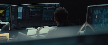 Movie still from “Kandahar” (2023), directed by Ric Roman Waugh – A man sitting in front of a computer monitor; Medium shot, Over the shoulder angle