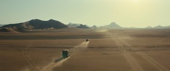 Movie still from “Kandahar” (2023), directed by Ric Roman Waugh – A truck driving down a dirt road in the middle of the desert; Extreme Wide shot, High angle