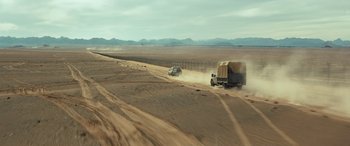 Movie still from “Kandahar” (2023), directed by Ric Roman Waugh – A truck driving down a dirt road next to a fence; Extreme Wide shot, High angle