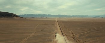 Movie still from “Kandahar” (2023), directed by Ric Roman Waugh – A dirt road going through the middle of the desert; Extreme Wide shot, High angle